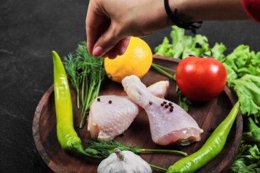 Elinde ahşap bir tabak dolusu taze sebzeli tavuk bacağı tutan bir kadın.