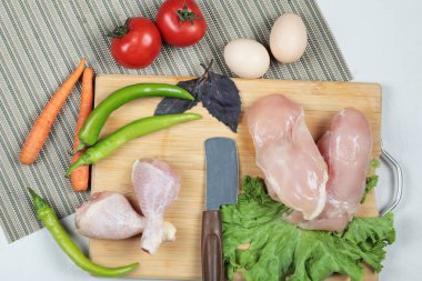 Çiğ tavuk budu ve fileto tahtada bıçak, yumurta ve taze sebzelerle.