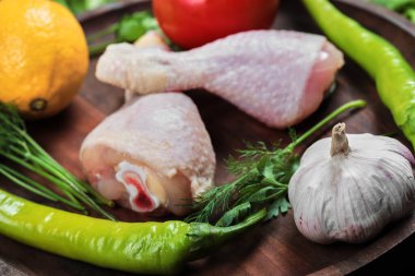 Tahta tabakta çiğ tavuk budu yeşillik, domates, sarımsak, biber ve limon.