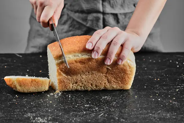 Жінка ріже хліб з ножем на темному столі — стокове фото