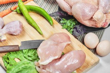 Çiğ tavuk budu ve fileto tahtada bıçak, yumurta ve taze sebzelerle.