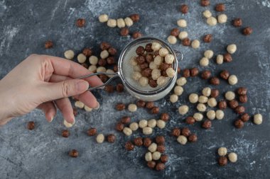 Süzgeç kaşığı dolusu mısır gevreği tutan bir kadın.