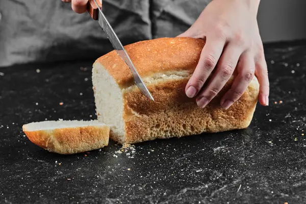 Kobieta krojąca chleb nożem na ciemnym biurku — Zdjęcie stockowe