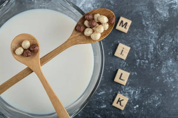 Bowl of milk, wooden letters and spoon of cereal balls on marble background