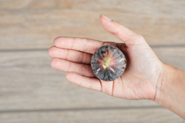 Ahşap bir arka planda mor bir incir tutuyor.