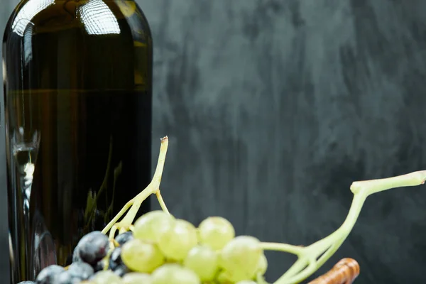 Uma garrafa escura de vinho com uvas ao redor — Fotografia de Stock