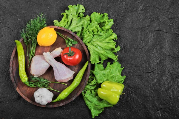 用青菜、西红柿、大蒜、辣椒和柠檬在木制盘子里切鸡腿 — 图库照片