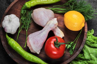 Tahta tabakta çiğ tavuk budu yeşillik, domates, sarımsak, biber ve limon.