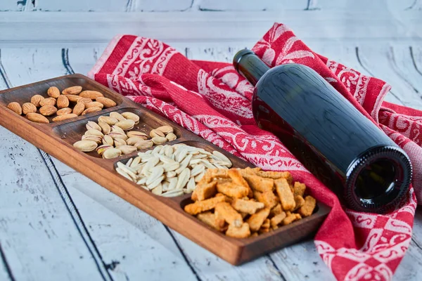 Aperitivos surtidos y una botella de vino en la mesa azul. Galletas saladas, semillas de girasol, pistachos, almendras — Foto de Stock