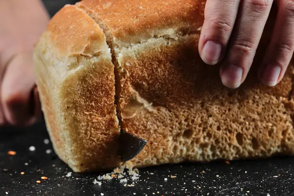 Mulher cortando pão com faca na mesa escura — Fotografia de Stock