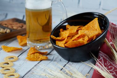 Bir kase cips ve mavi masada bir bardak bira.