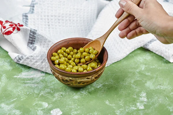 Ręka biorąc łyżkę gotowanego zielonego groszku na zielonym stole — Zdjęcie stockowe