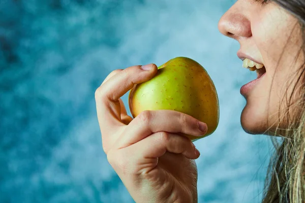 Женщина ест яблоко на голубом фоне — стоковое фото