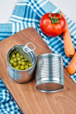 İki kutu haşlanmış yeşil bezelye, sebze ve masa örtüsü beyaz arka planda.