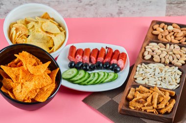 Pembe masada çeşitli atıştırmalıklar. Cips, sosis, fıstık, zeytin