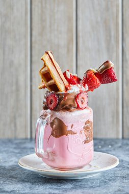 Koyu mavi arka planda beyaz tabakta küçük waffle, çikolata ve çilek dilimleri ile çilekli smoothie