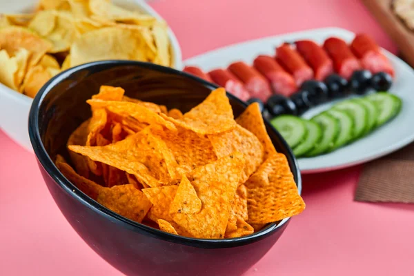 Duas taças de batatas fritas e chapa de salsicha com fatias de pepino e azeitonas na mesa rosa — Fotografia de Stock