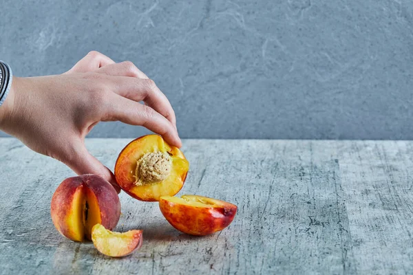 Hand innehav halv styckning av persika på marmor bakgrund — Stockfoto