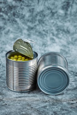 Bir mermer zeminde iki kutu haşlanmış yeşil bezelye.