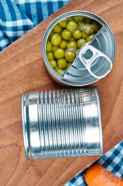 Ahşap bir tahtanın üzerinde iki kutu haşlanmış yeşil bezelye sebze ve masa örtüsü.