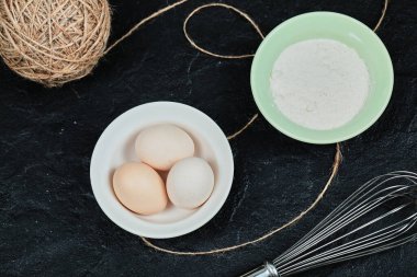 Seramik tabakta tavuk yumurtası ve bıyıklı bir kase un.