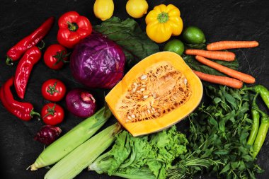 Yarısı kesilmiş balkabağı ve siyah masada taze sebzeler.