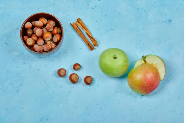 Manzanas, canela y tazón de avellanas sobre fondo azul — Foto de Stock
