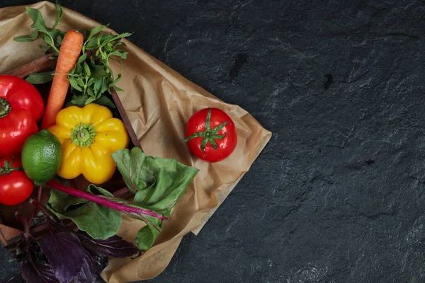 Peppers, lime, carrot, tomatoes and greens in wooden box on dark background — Stock Photo, Image