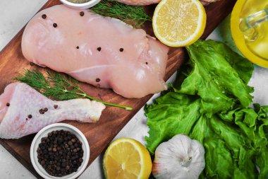 Çiğ tavuk fileto ve bacaklar taze sebze ve baharatla ahşap tabakta.