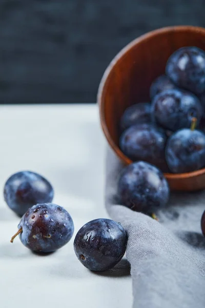 Prunes mûres dans un bol avec nappe grise sur table blanche — Photo