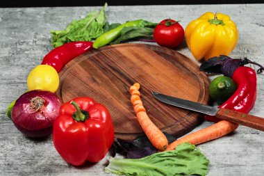 Biberler, yeşiller, limon, domates ve havuç ahşap tabağın etrafında mermer arka planda.