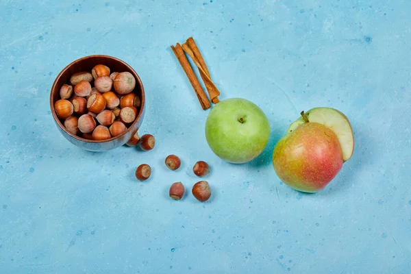 Manzanas, canela y tazón de avellanas sobre fondo azul — Foto de Stock