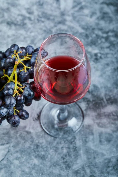 Una copa de vino tinto sobre un fondo de mármol con uvas —  Fotos de Stock