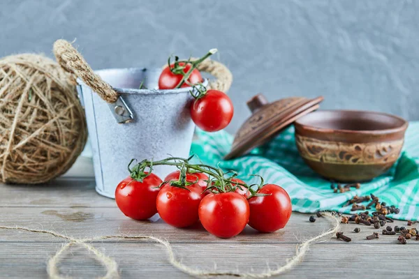 Eimer mit Tomaten und Nelken auf Holztisch mit leerer Schüssel — Stockfoto