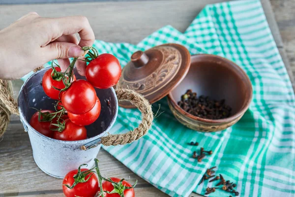 Hand hält Tomaten auf Holztisch mit einer Schüssel Nelken — Stockfoto