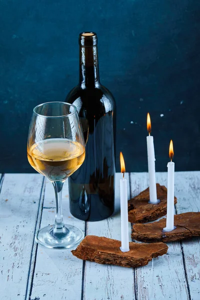 A glass of white wine and bottle on blue table with candles — Stock Photo, Image