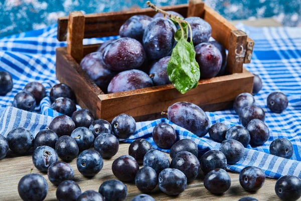 Wooden basket of garden plums on a wooden table with a tablecloth — Stock Photo, Image