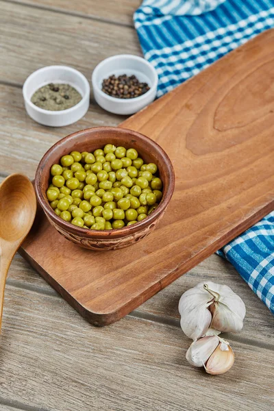 Miska gotowanego zielonego groszku z łyżką, przyprawami, czosnkiem i niebieskim obrusem na drewnianym stole — Zdjęcie stockowe