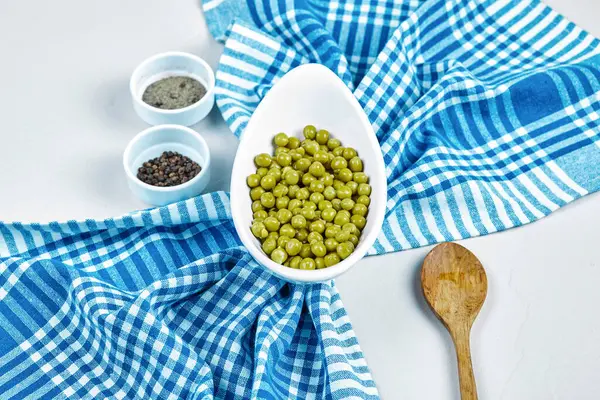 Gotowany zielony groszek w białej misce na białym tle z przyprawami, łyżką i obrusem — Zdjęcie stockowe