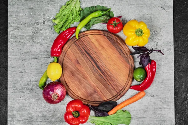 Peperoni, verdure, limone, pomodoro e carota attorno al piatto di legno su fondo di marmo — Foto Stock