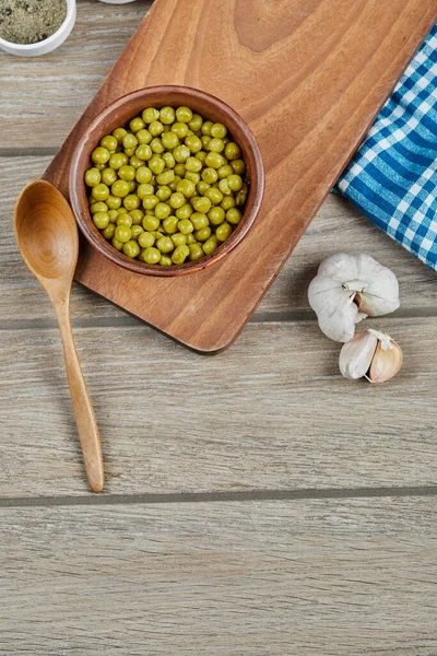 Miska gotowanego zielonego groszku z łyżką, czosnkiem i niebieskim obrusem na drewnianym stole — Zdjęcie stockowe
