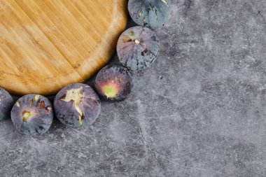 Ahşap bir tabağın etrafında mermer bir zemin üzerinde mor incirler.