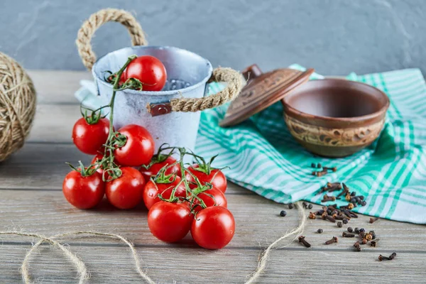 Eimer mit Tomaten und Nelken auf Holztisch mit leerer Schüssel — Stockfoto