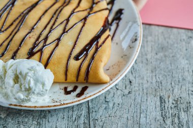 Vanilyalı dondurmalı krep, mermer kaplamalı beyaz tabakta çikolata.