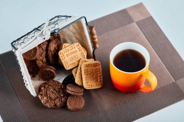 Çeşitli bisküviler, şekerler ve gri arka planda bir fincan çay.