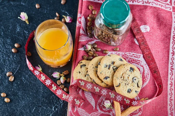 Chocolate chips cookies, coffee beans in a glass jar and a glass of orange juice on dark table — Stock Photo, Image