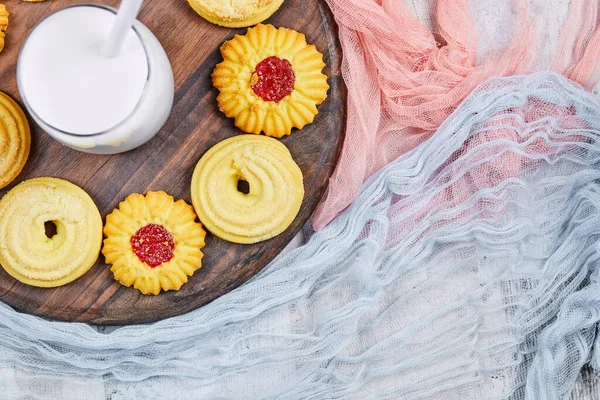 Gesorteerde koekjes en een pot melk op een houten bord met tafelkleden — Stockfoto