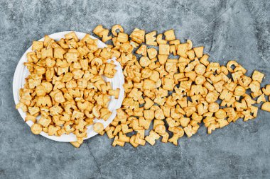 Beyaz bir tabakta ve mermer bir zeminde dağılmış alfabe krakerleri.