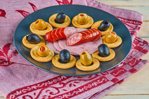 粉红桌布陶瓷盘上的饼干环和橄榄香肠片 — 图库照片