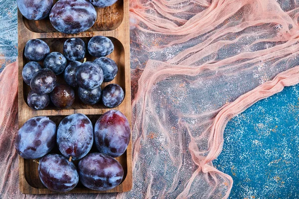 Prunes de jardin sur plateau en bois et sur fond bleu avec nappes — Photo